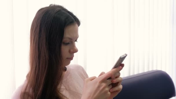 Jovem morena está digitando uma mensagem em seu telefone celular e olhando para a tela. Vista lateral . — Vídeo de Stock