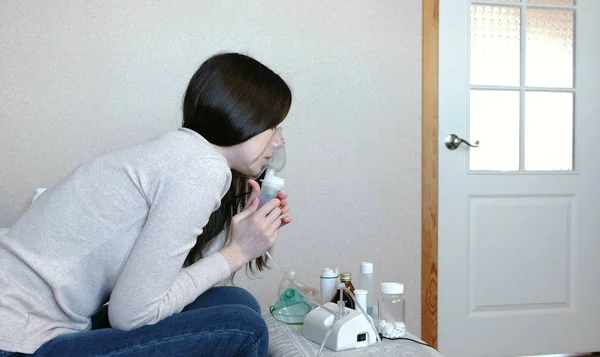 W leczeniu za pomocą rozpylacza i inhalator. Młoda kobieta wdechu przez inhalator maski. Widok z boku. — Zdjęcie stockowe