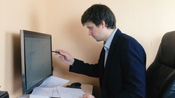 Muž pracuje na počítači. Porovnává grafiku na obrazovce a na papíře. — Stock video