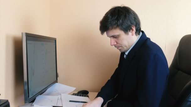 Hombre frustrado trabajando en la computadora y llamando al teléfono móvil. Compara gráficos en la pantalla y en papel . — Vídeos de Stock