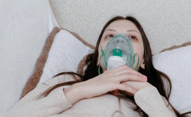 Nebulizatör ve astım tedavisi için kullanın. Closeup genç kadın kanepede yatan inhaler maskesi aracılığıyla teneffüs edilmesi. Önden Görünüm.