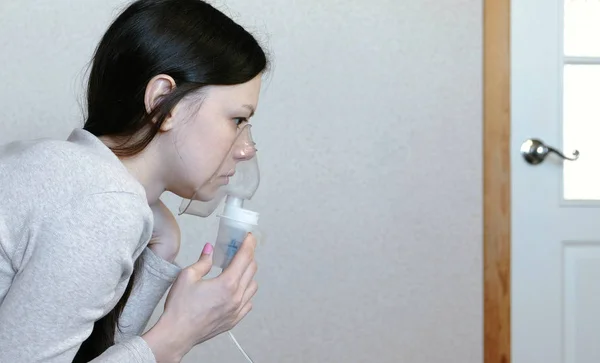 Use nebulizador e inalador para o tratamento. Mulher jovem inalando através da máscara do inalador. Vista lateral close-up . — Fotografia de Stock