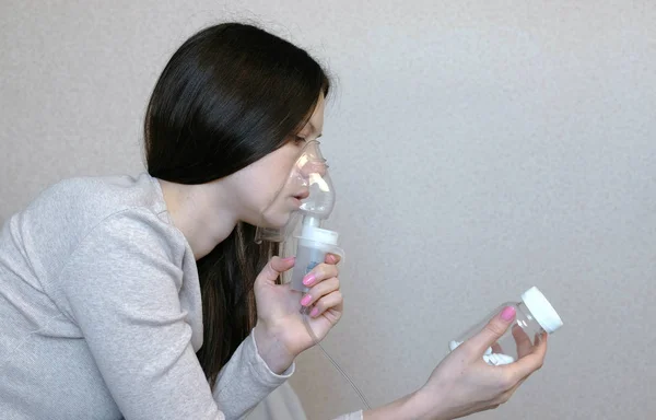 Nebulizatör ve astım tedavisi için kullanın. Genç kadın inhaler maskesi teneffüs edilmesi bir şişe hap görünüyor. Yan görünüm. — Stok fotoğraf