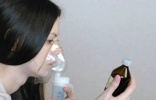 Use nebulizador e inalador para o tratamento. Jovem mulher inalando através de máscara inalador olha para um frasco de comprimidos. Vista lateral close-up . — Fotografia de Stock