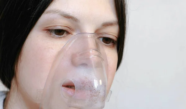Use nebulizer and inhaler for the treatment. Closeup young womans face inhaling through inhaler mask. Front view