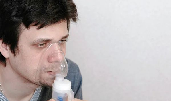 Vernevelaar en inhalator gebruiken voor de behandeling. Closeup jonge mans gezicht inademen door inhalator masker. Zijaanzicht. — Stockfoto