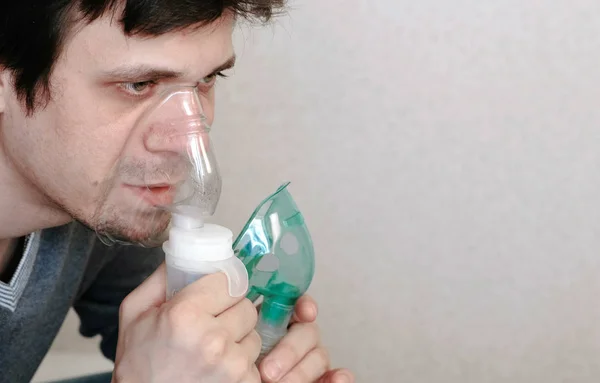 Use nebulizer and inhaler for the treatment. Closeup young mans face inhaling through inhaler mask. Side view