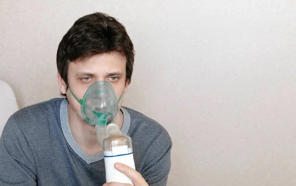Vernevelaar en inhalator gebruiken voor de behandeling. Closeup jonge mans gezicht inademen door inhalator masker. Vooraanzicht — Stockfoto