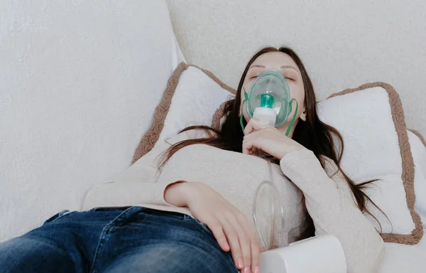 Nebulizatör ve astım tedavisi için kullanın. Genç kadın kanepede yatan inhaler maskesi aracılığıyla teneffüs edilmesi. Önden Görünüm. — Stok fotoğraf