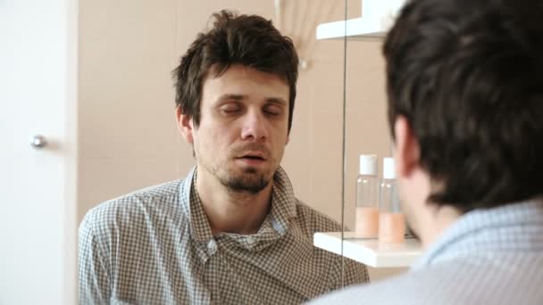 El hombre cansado que acaba de despertarse mira su reflejo en el espejo casi dormido de pie. Vestido con una camisa a cuadros . — Vídeos de Stock