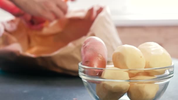 Картошка в миске. Чистый картофель. Манские руки чистят картофель в экопакете на заднем плане . — стоковое видео