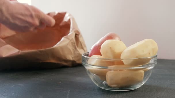 Potatisen i en skål. Skalad potatis. Mans händer rengöring potatis i en eco bag i bakgrunden. — Stockvideo