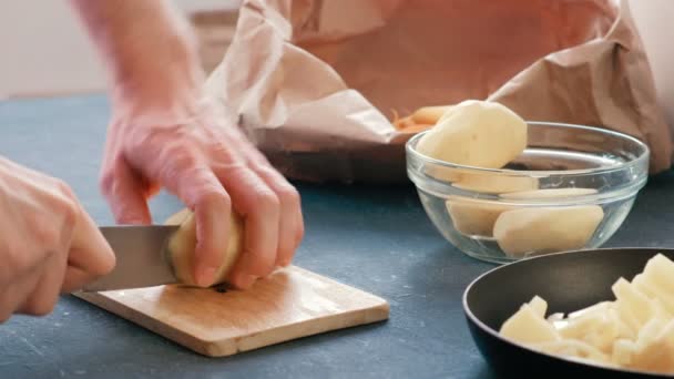 Mãos de homem de close-up que cortam uma batata em uma tábua de madeira e o põem em uma panela de ato de fritar com o óleo . — Vídeo de Stock