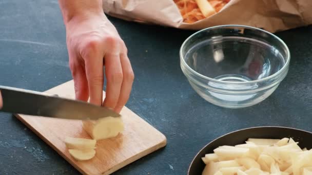 Tangan yang tertutup memotong kentang di papan kayu dan meletakkannya di atas wajan dengan minyak . — Stok Video