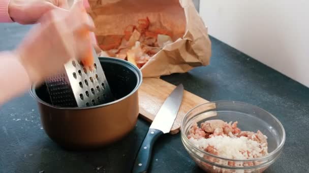 Κοντινό πλάνο γυναικεία χέρια τρίβει τα καρότα σε ένα τρίφτη στην κατσαρόλα. — Αρχείο Βίντεο