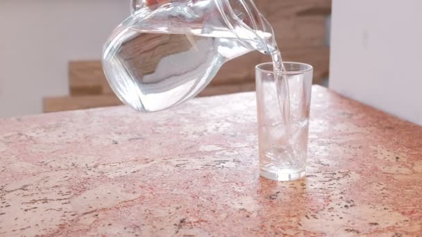 Крупным планом человек вручную заливает воду из графина в стекло и берет стакан . — стоковое видео
