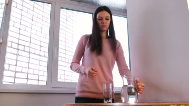 Ung kvinna hälla vatten från från karaff i glas och dricker det. — Stockvideo