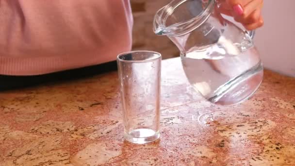Mãos de mulher de close-up derramando uma água de decantador para vidro e leva um copo . — Vídeo de Stock