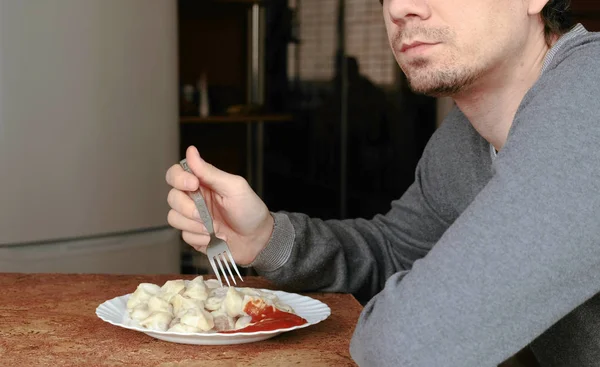Неузнаваемый человек ест пельмени вилкой, кладя их в томатный соус на кухне. . — стоковое фото