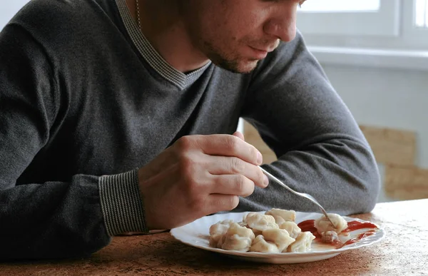 Неузнаваемый человек ест пельмени вилкой, кладя их в томатный соус на кухне. . — стоковое фото