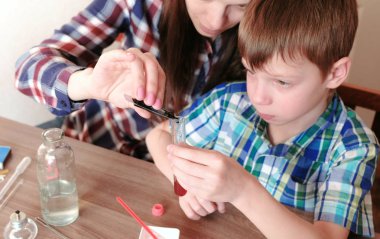 Kimya deneyleri evde. Anne kırmızı sıvı ile test tüpü mavi boya bir damla ekler.