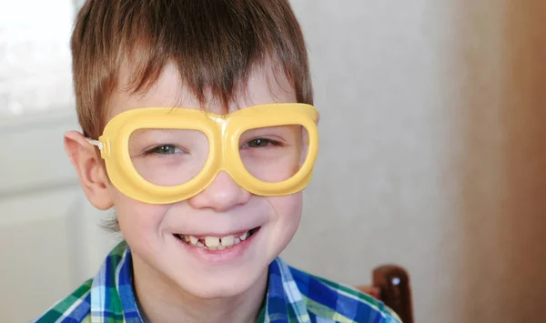 Niño sonriente con gafas amarillas de seguridad sentado en la mesa y mirando a la cámara. Experimentos de química en casa . — Foto de Stock