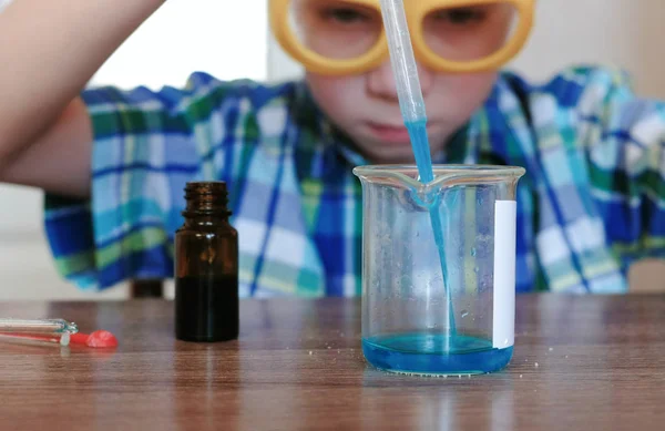 Expériences en chimie à la maison. Garçon verse liquide bleu d'un bocal dans un bécher avec une pipette . — Photo