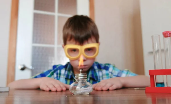 Experimenten op chemie thuis. Jongen kijkt de brandende alcohol lamp in vuur en vlam met een wedstrijd. — Stockfoto