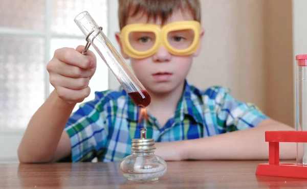 Experimentos de química en casa. Chico calienta el tubo de ensayo con líquido rojo en la lámpara de alcohol ardiente . — Foto de Stock