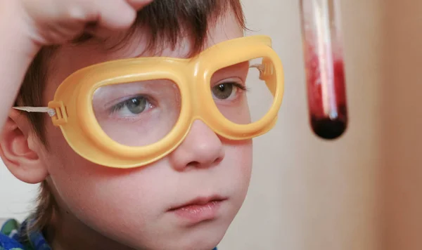 Expériences en chimie à la maison. Gros plan Le visage des garçons examine le contenu de l'éprouvette . — Photo