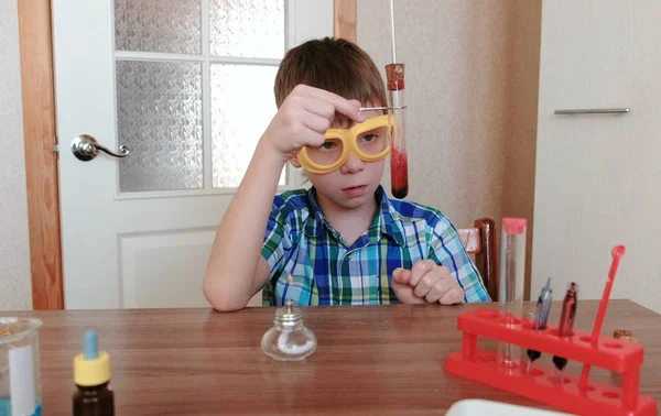 Experiências de química em casa. Rapaz examina o conteúdo do tubo de ensaio . — Fotografia de Stock