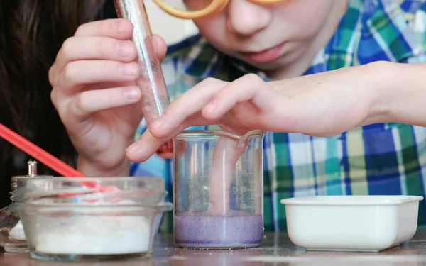 Πειράματα χημείας στο σπίτι. Το αγόρι αγγίζει το υγρό στο δοχείο με το δάχτυλό του. — Φωτογραφία Αρχείου