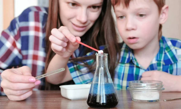 Scheikundige experimenten thuis. Moeder en zoon maken een chemische reactie met de release van gas in de kolf. — Stockfoto