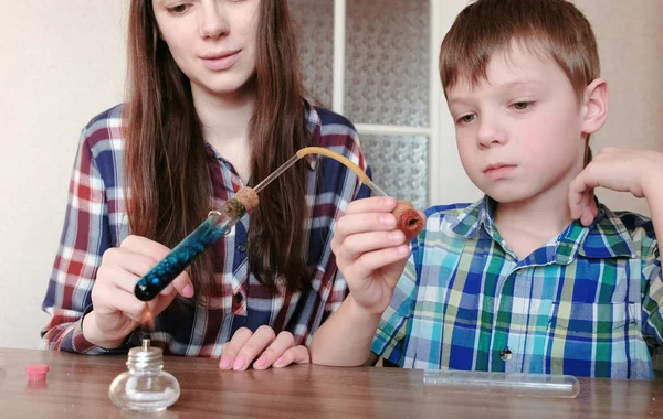 Experimentos de química en casa. Boy y su mamá calientan el tubo de ensayo con líquido azul en la lámpara de alcohol en llamas . —  Fotos de Stock