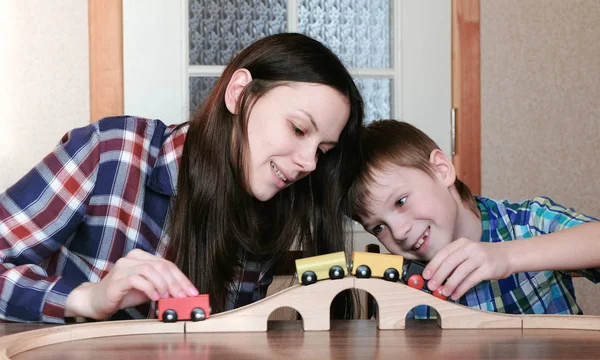 Együtt játszottak. Boldog anya és fia játszik egy fából készült vasúti vonat, a vagonok és a alagút ült az asztalnál. — Stock Fotó