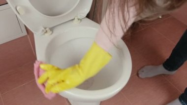 Sarı lastik eldiven eller kadının tuvalete pembe bez ile silin ve tuvalet yıkamak.