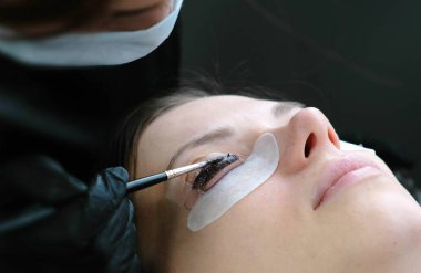 Güzellik bakımı. Güzellik uzmanı siyah boya kirpiklere üzerinde koyar. Botox ve kirpik laminasyon. Portre yüz yan görünüm.