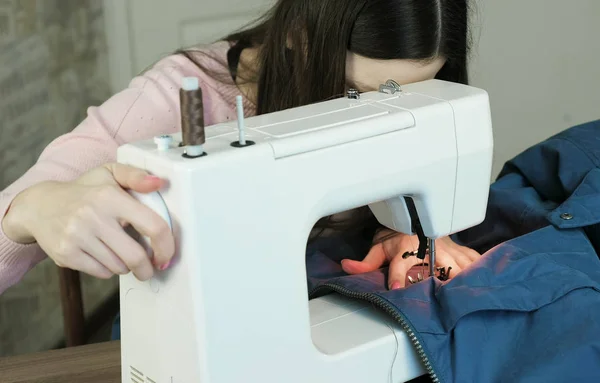 Young woman sews blue jacket on white sewing mashine. — Stock Photo, Image