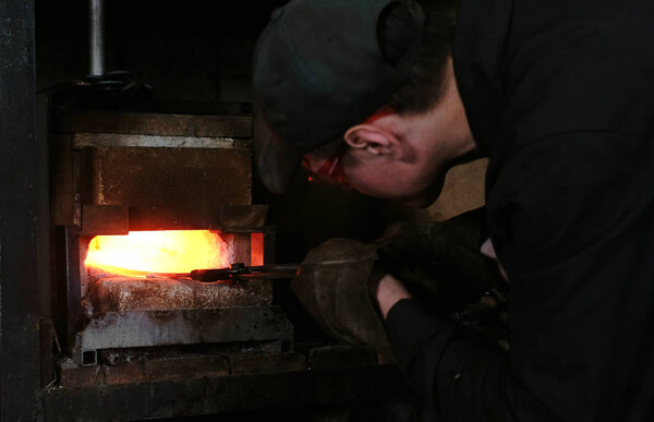 Making the sword out of metal at the forge. Blacksmith pulls out of the furnace hot metal blanks.