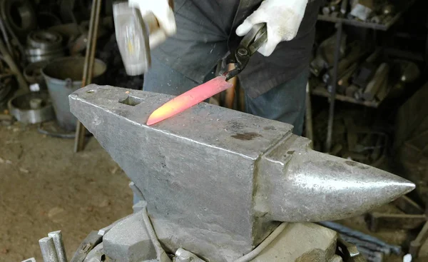 Het maken van het mes uit metaal in de smidse. Close-up van smeden handen raken van ruwijzer met een enorme hamer op een aambeeld. — Stockfoto
