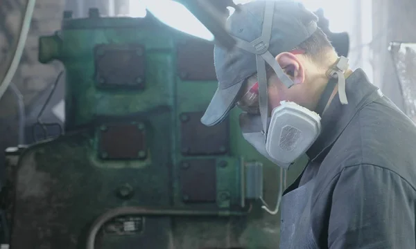 Trabalhador executa seu trabalho em uma máscara protetora em seu rosto na loja entre os equipamentos . — Fotografia de Stock