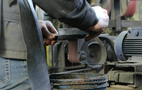Moagem de tarugos de faca de metal em uma máquina de moagem de cinto. Close-up de um homem mãos . — Fotografia de Stock