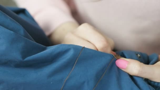 Nahaufnahme einer Frauenhand, die von Hand einen Ledereinsatz an eine blaue Jacke näht. — Stockvideo