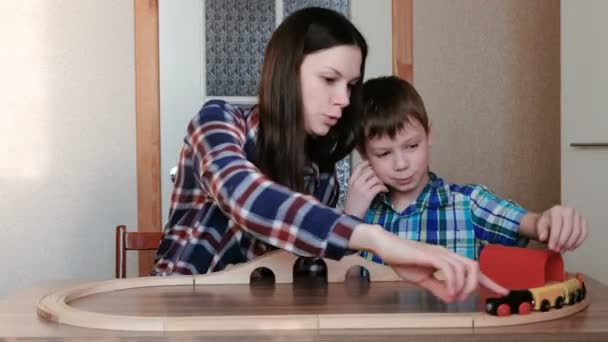 Spela tillsammans. Mamma och son spelar en träjärnväg med tåg, vagnar och tunneln som sitter vid bordet. — Stockvideo
