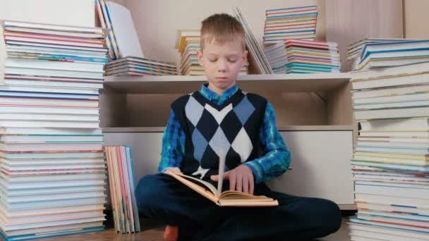 Siebenjähriger Junge liest aufmerksam zwischen Büchern sitzend. — Stockvideo