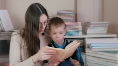 Anne bardaklarda kitaplar arasında oturan oğlu için bir kitap okuma.