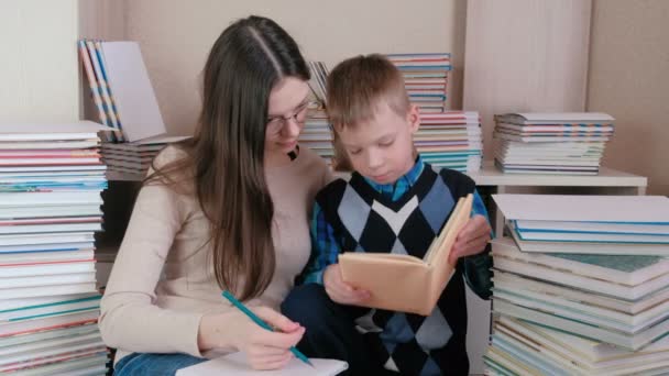 Mom and son read a book together. Mom in glasses writes something in a notebook. — Stock Video