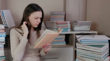 Gözlüklü genç esmer kadın kitap kitaplar arasında katta oturan okumak.