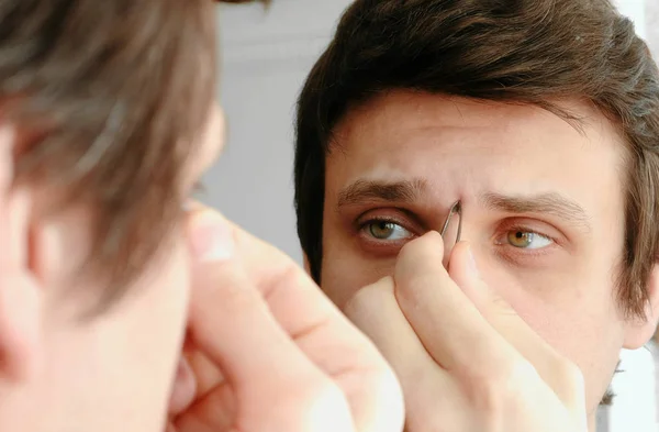 Young man plucking his eyebrows with tweezers. Styling eyebrows. — Stock Photo, Image
