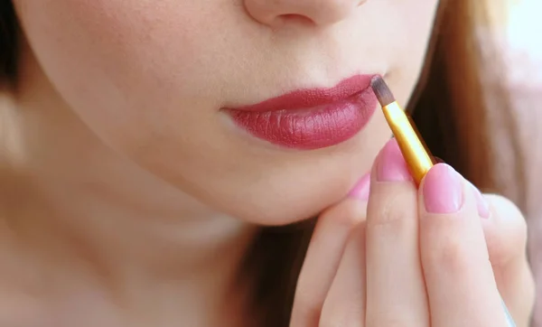 Primer plano de una mano de mujer con un pincel que pone lápiz labial brillante en sus labios . —  Fotos de Stock